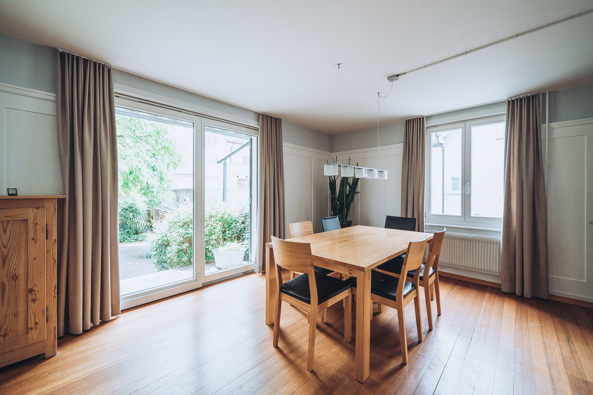 Ansicht einer Wohnungseinrichtung mit Holzm&ouml;beln, gepolstertem Sofa und Vorh&auml;ngen